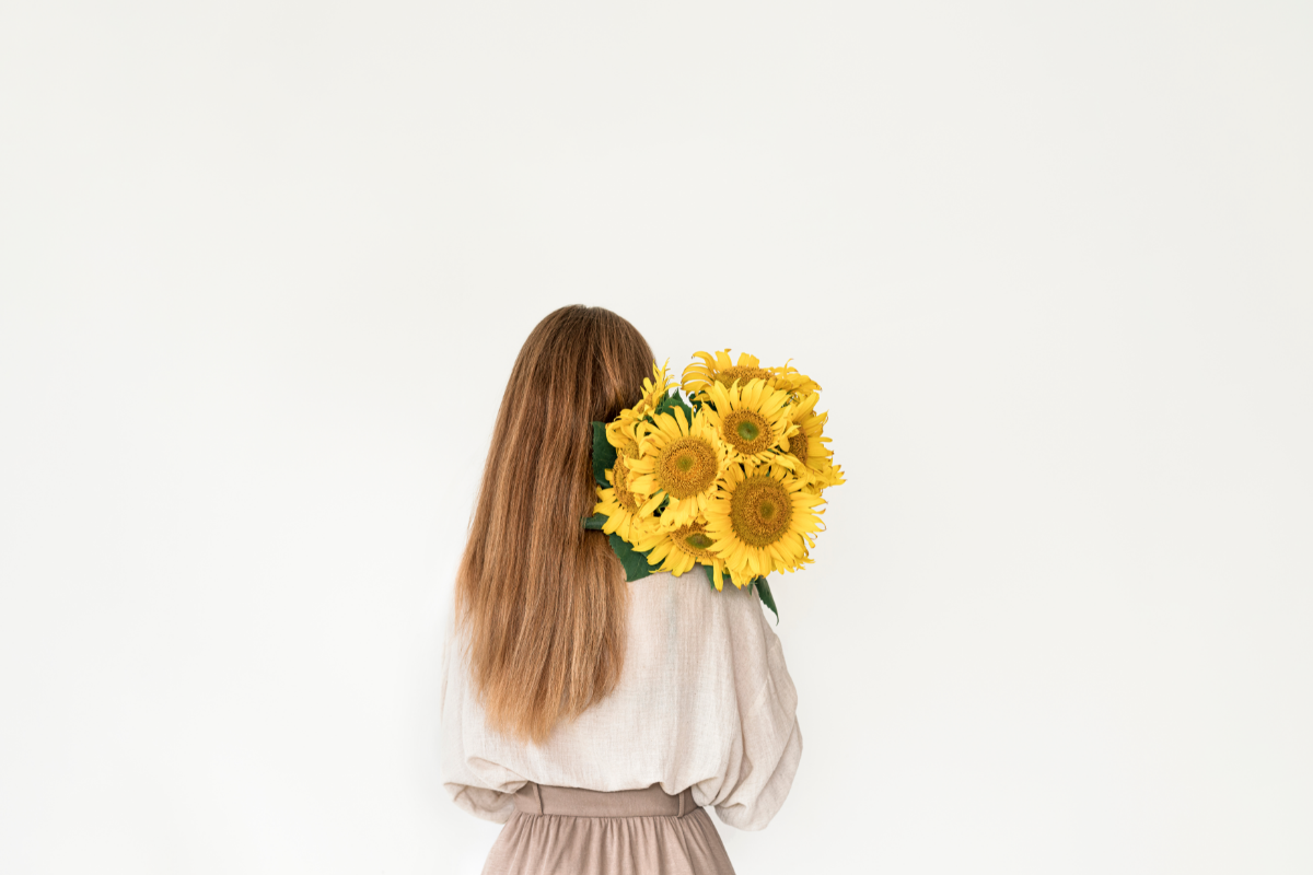 How to Switch to Sustainable & Ethical Fashion - Stock Image of a woman with her back to the camera wearing neutral coloured clothes, holding a bunch of sunflowers