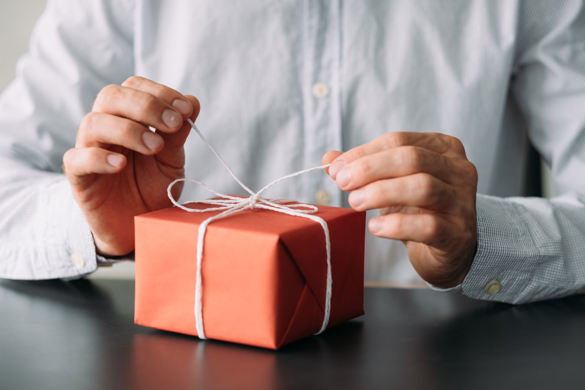 Eco-friendly Corporate Gifts - Stock feature image of someone in a formal shirt opening a gift wrapped matt paper and tied with paper ribbon