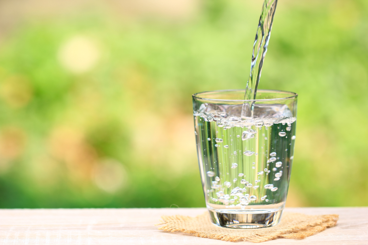 Water filter benefits - stock image of a clear glass with water pouring into it on an outdoor table with greenery in the background