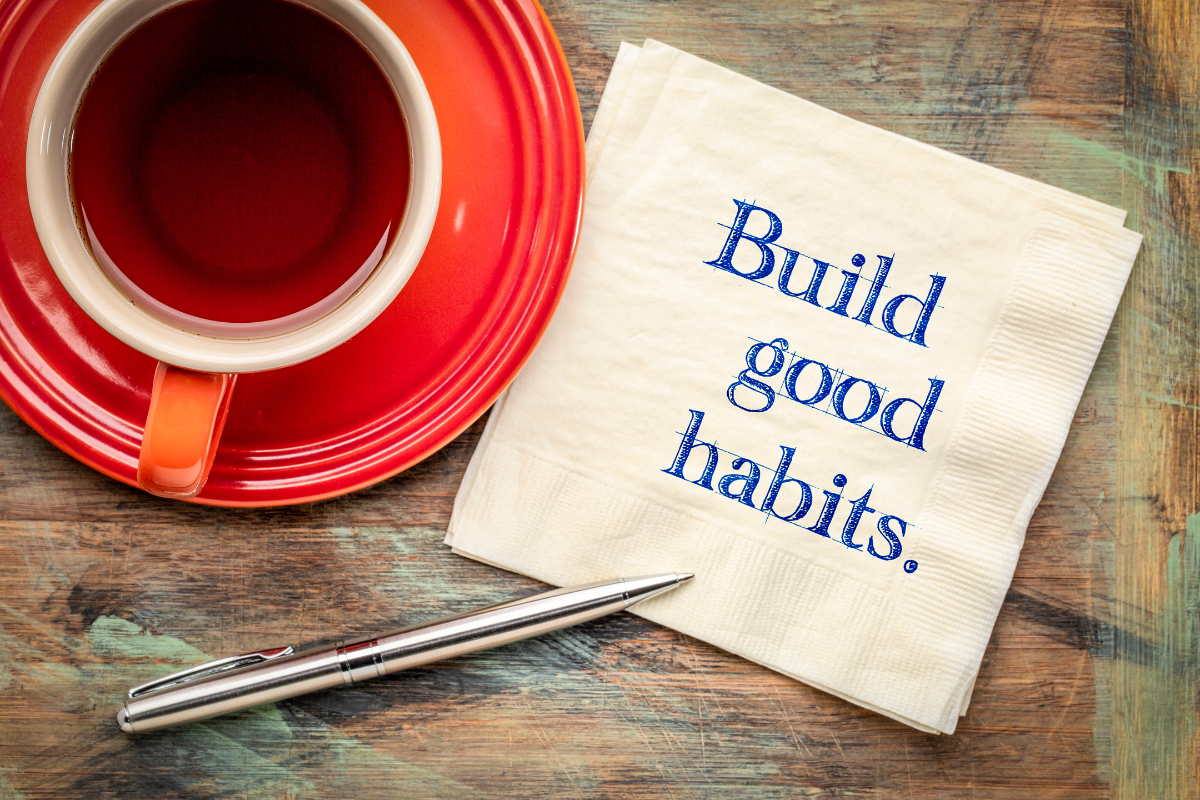 Sustainable Resolutions - Stock Feature Image from Canva. Image text says "build good habits" in blue ink in a while napkin, next to an orange cup and saucer with black coffee