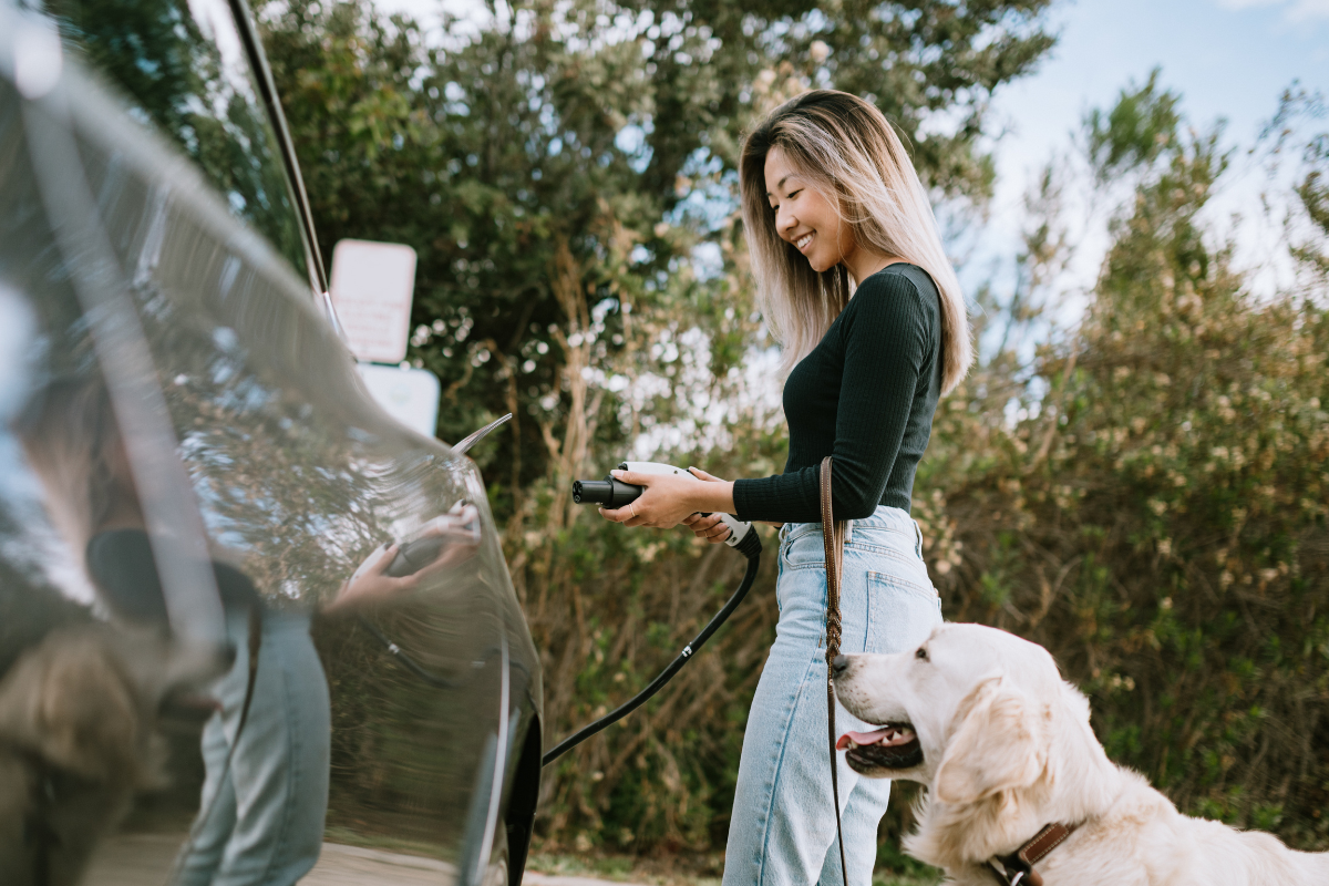 reasons to switch to an electric car - stock image from Canva of a woman and her labrador standing next to a charging vehicle